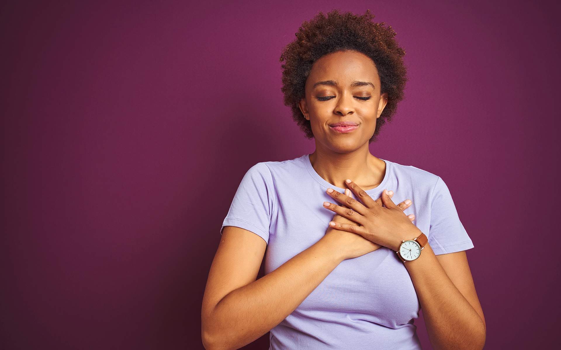 A 12-minute meditation for expanding our hearts - Young beautiful african american woman with afro hair over isolated purple background smiling with hands on chest with closed eyes and grateful gesture on face. Health concept.