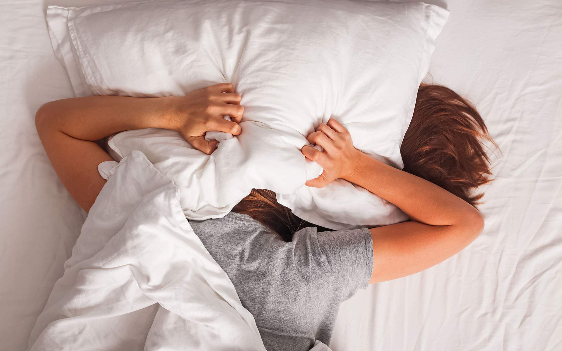 Why Can't I Sleep? 4 Tips for Better Rest - Woman lying in bed and covering her head with pillow.