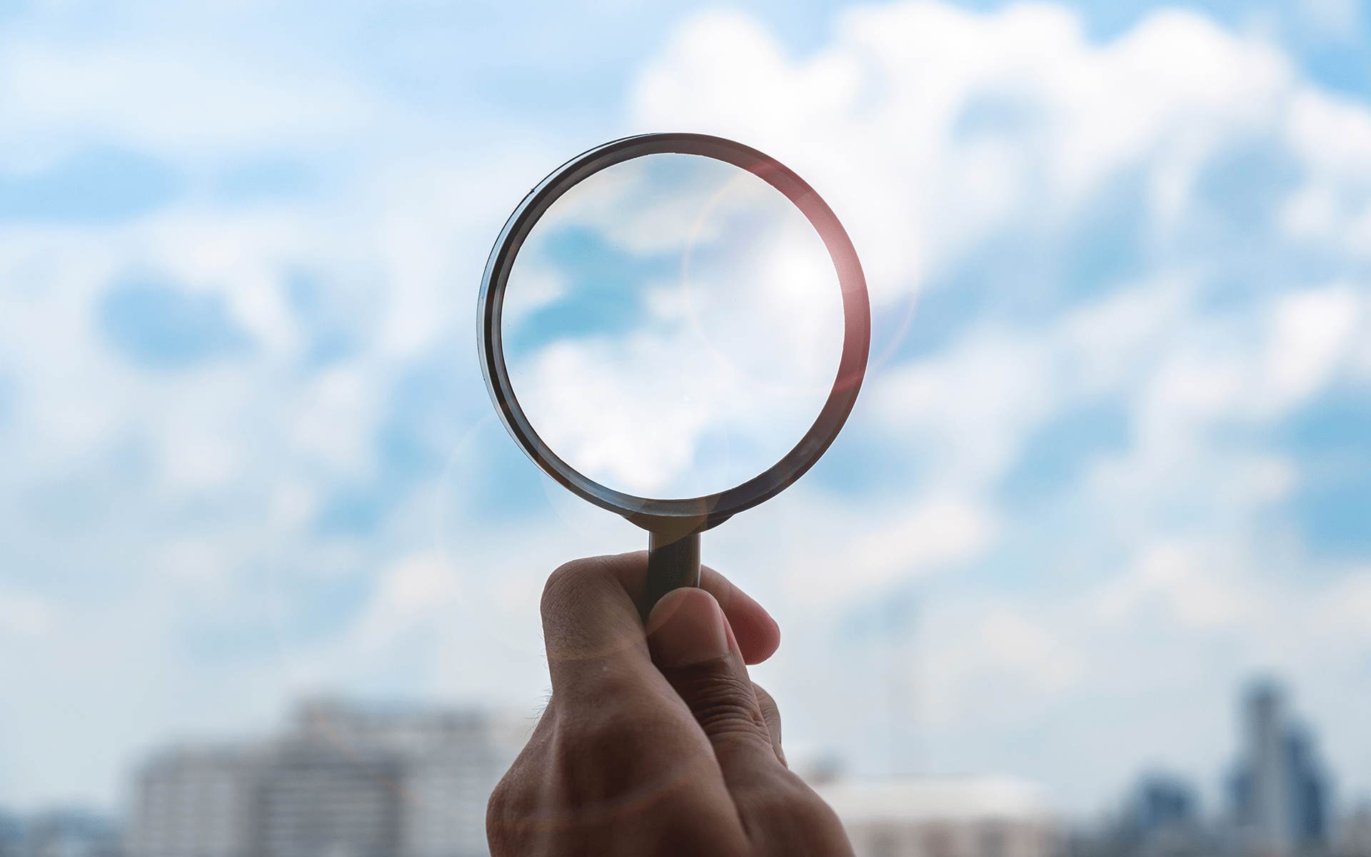一只手拿着玻璃放大镜对着蓝天背景