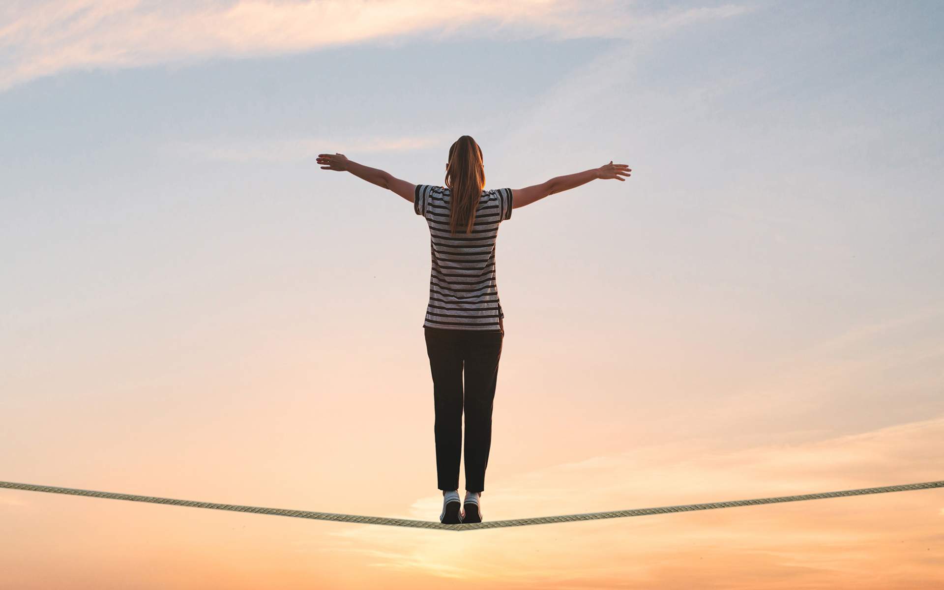 一个女孩站在绳子上，在夕阳下举起双手。自由的概念。